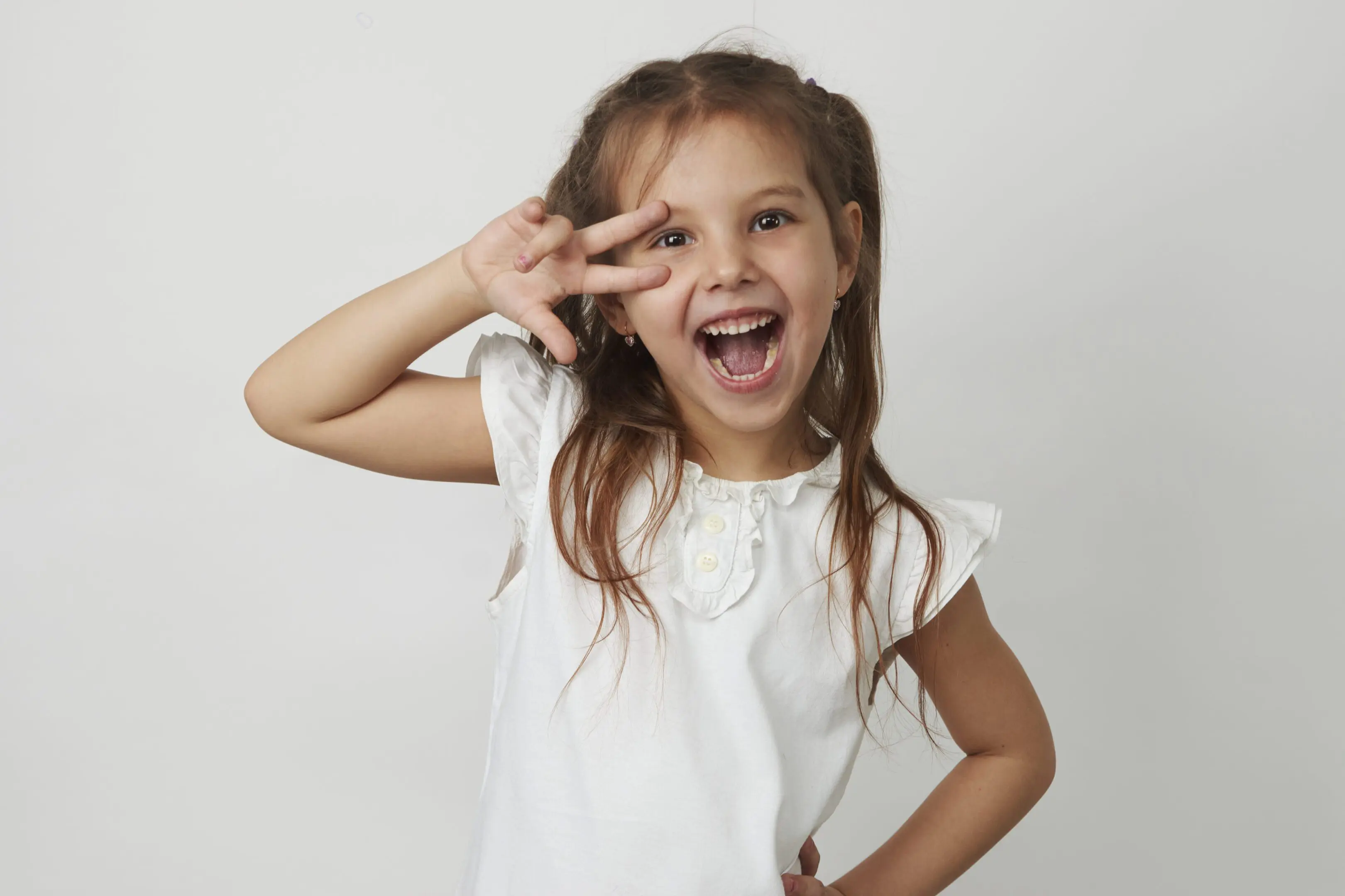 A joyful young girl making a playful peace sign near her eye.