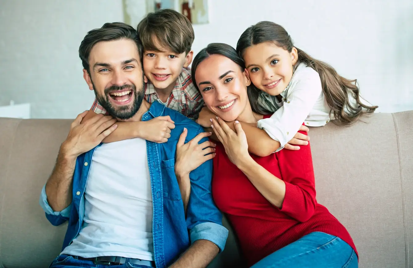 Happy family of four posing closely and smiling warmly.