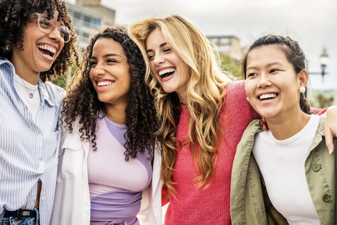Four diverse friends smiling and enjoying each other's company outdoors.